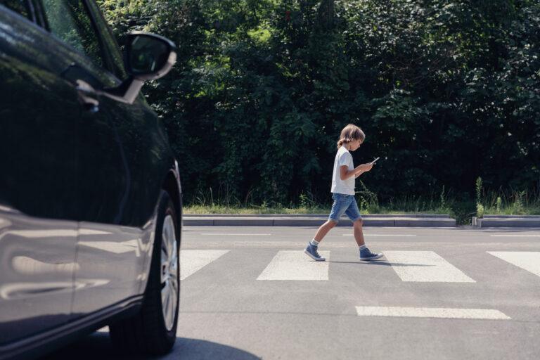 A child crosses the street looking at his phone moments before being injured by a reckless driver.